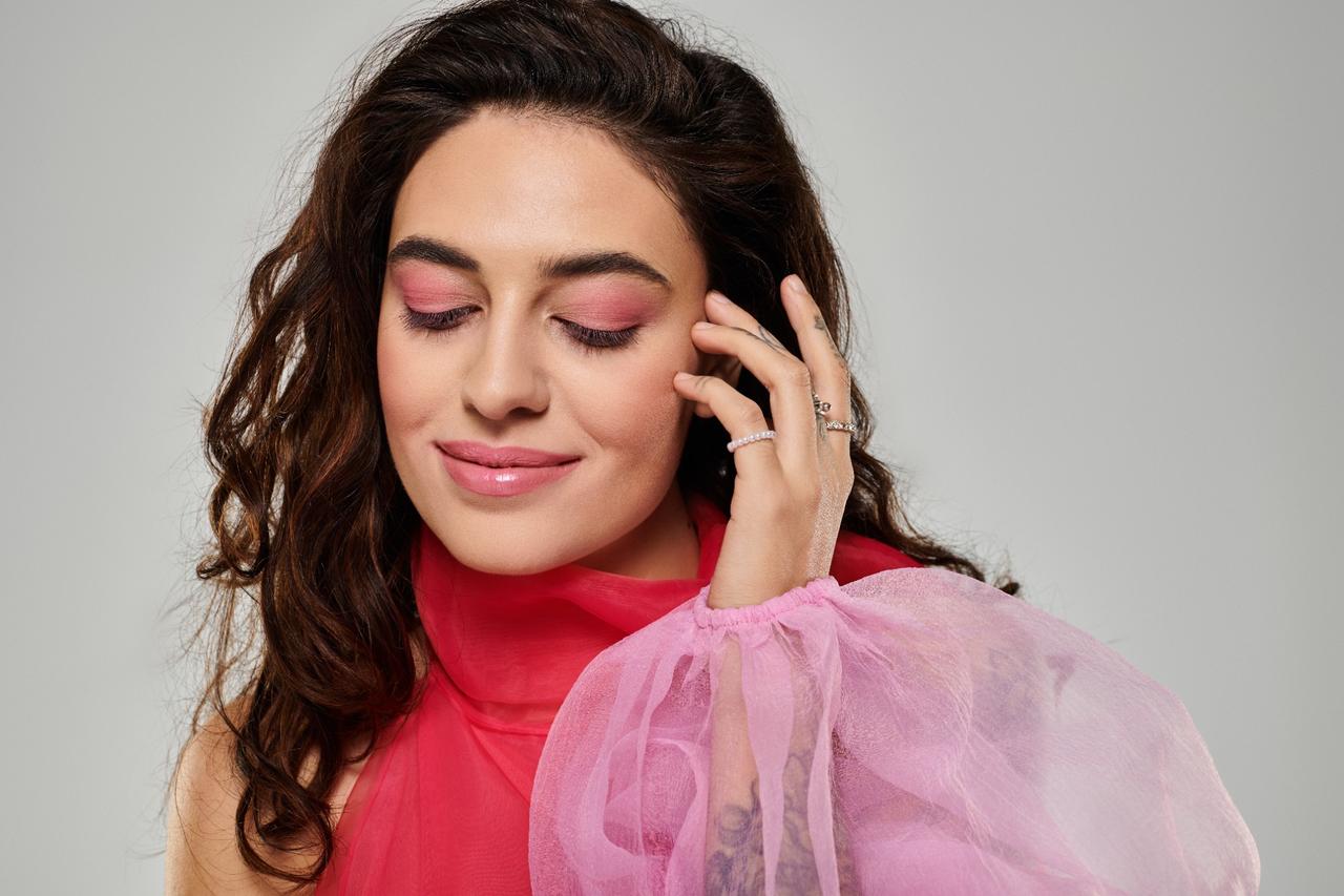 Model with soft pink eyeshadow, glossy lips, and elegant pink outfit smiling with eyes closed