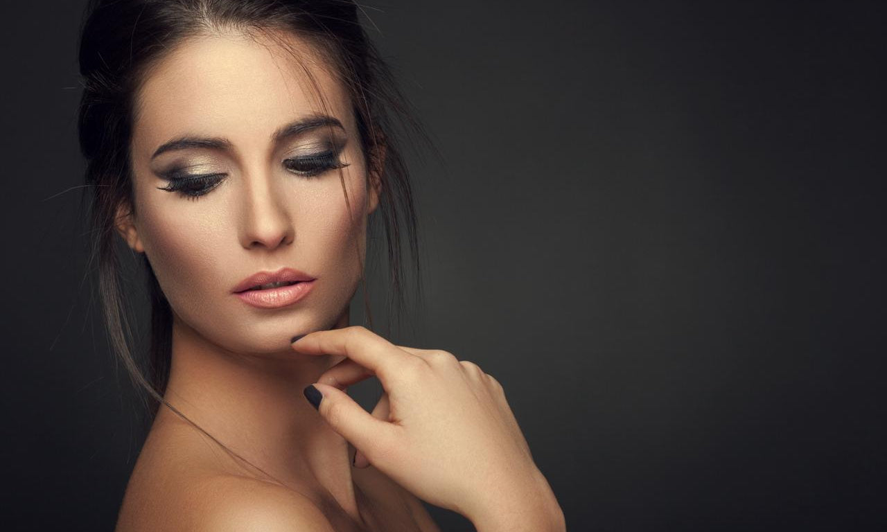 Close-up of woman with dramatic smokey eye makeup and nude lips against dark background