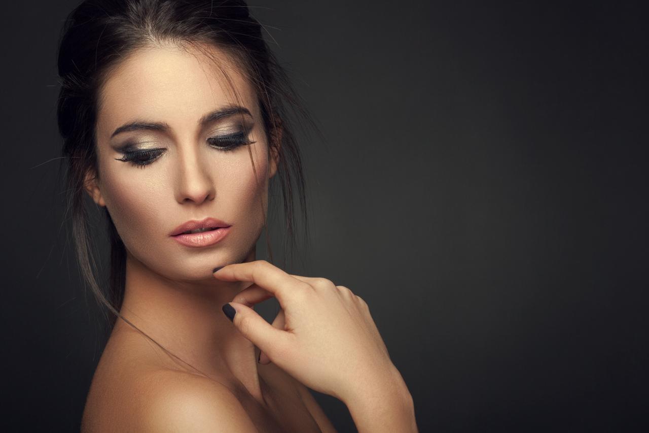 Close-up of woman with dramatic smokey eye makeup and nude lips against dark background