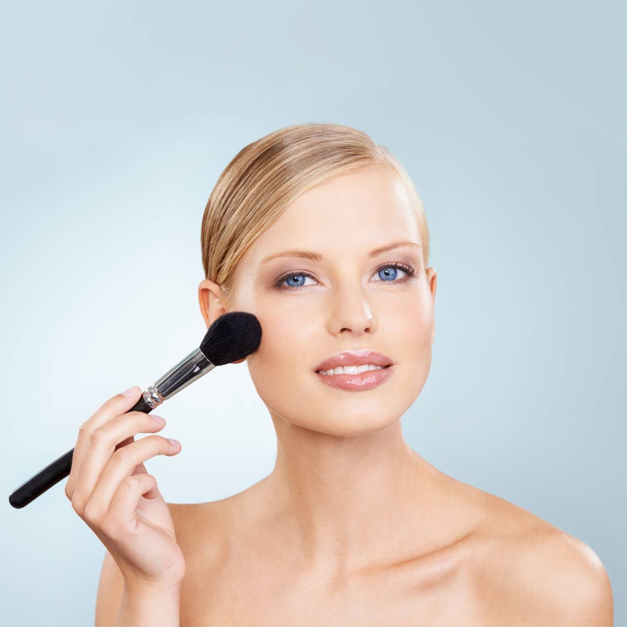 smiling woman applying face blush with a makeup brush for a natural glowing look