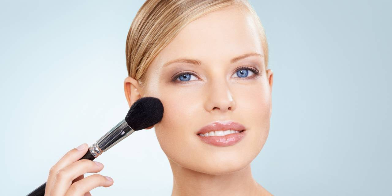 smiling woman applying face blush with a makeup brush for a natural glowing look