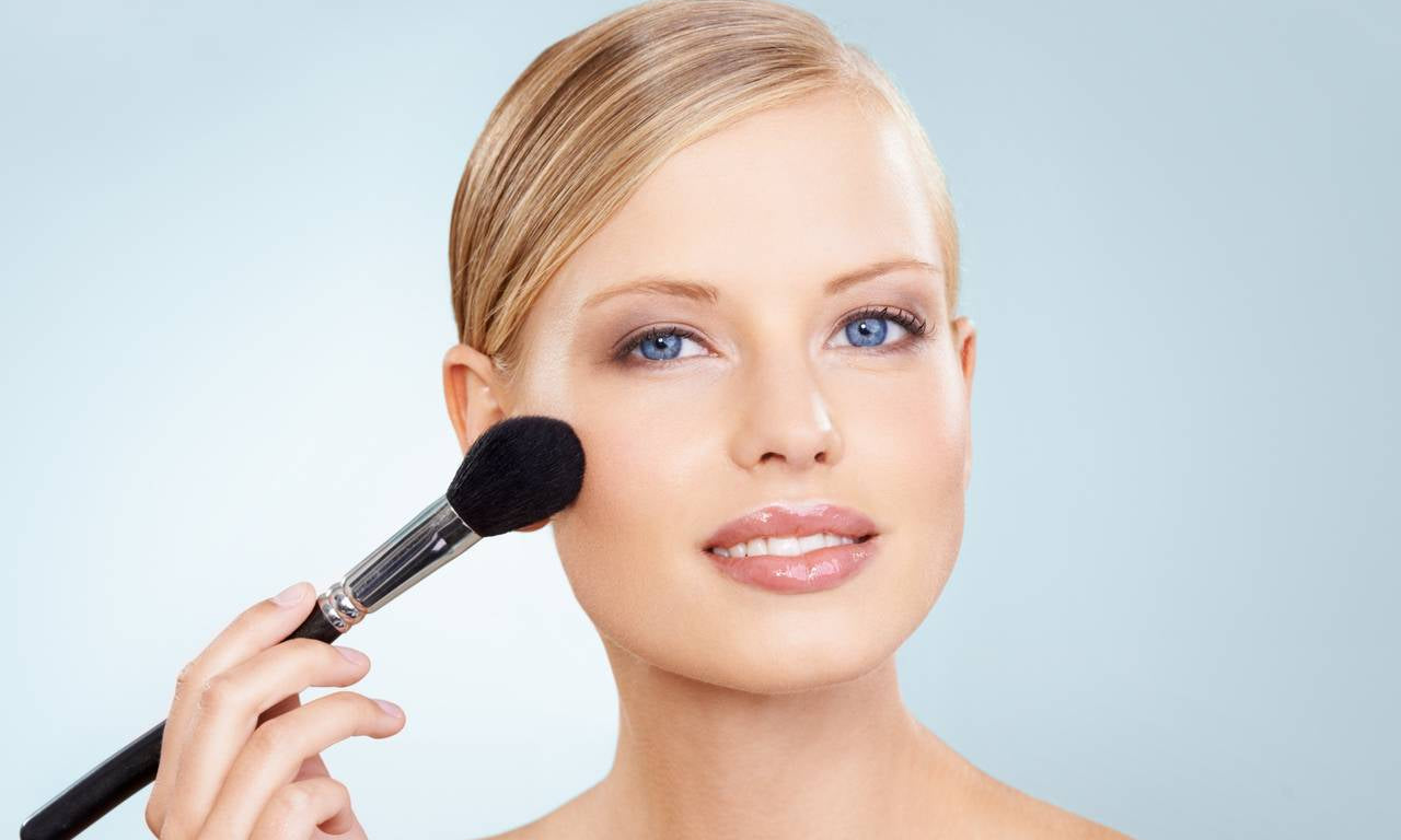smiling woman applying face blush with a makeup brush for a natural glowing look