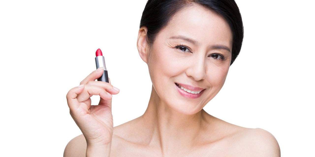 smiling woman holding red lipstick tube close to her face on white background