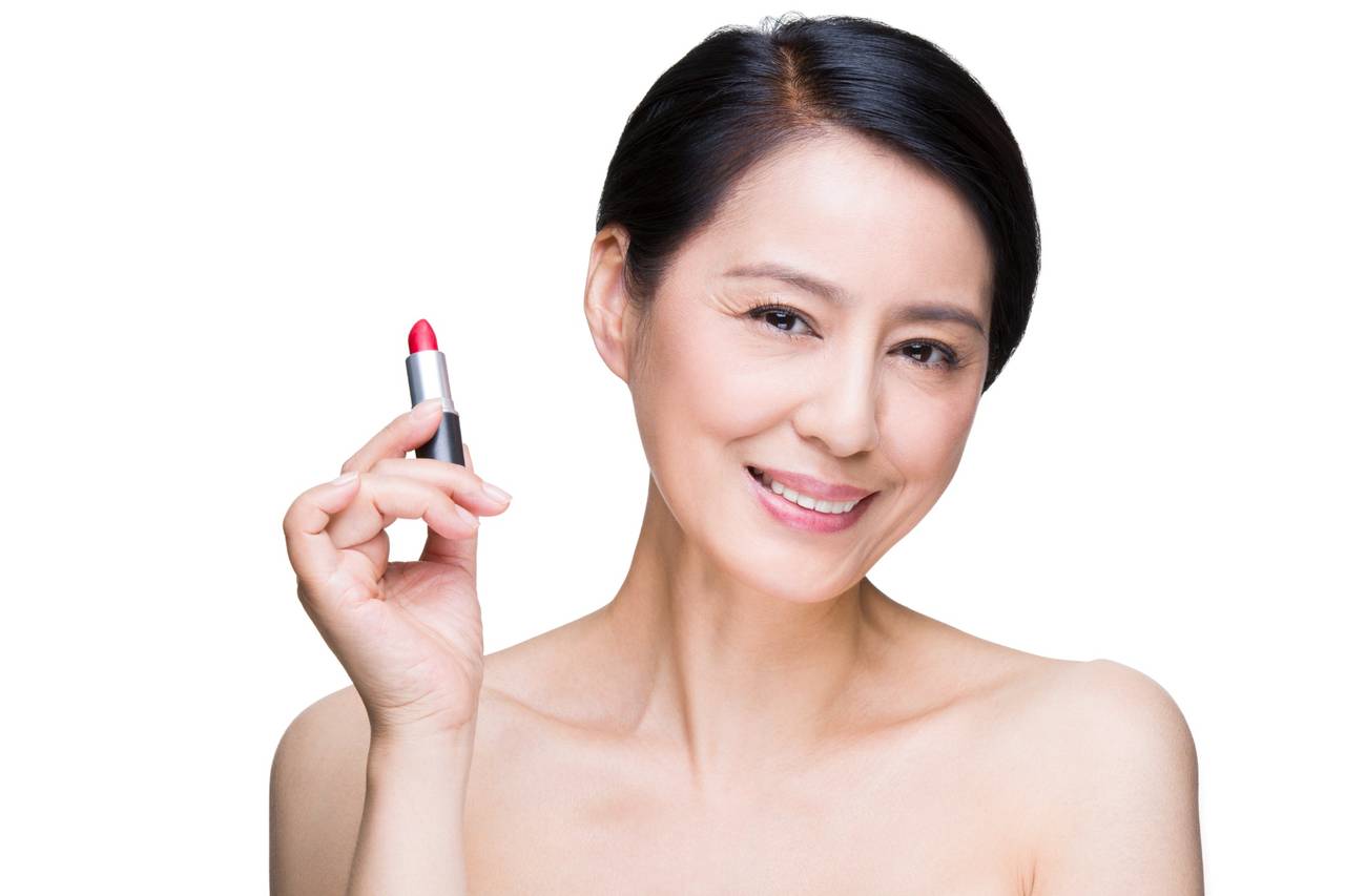 smiling woman holding red lipstick tube close to her face on white background