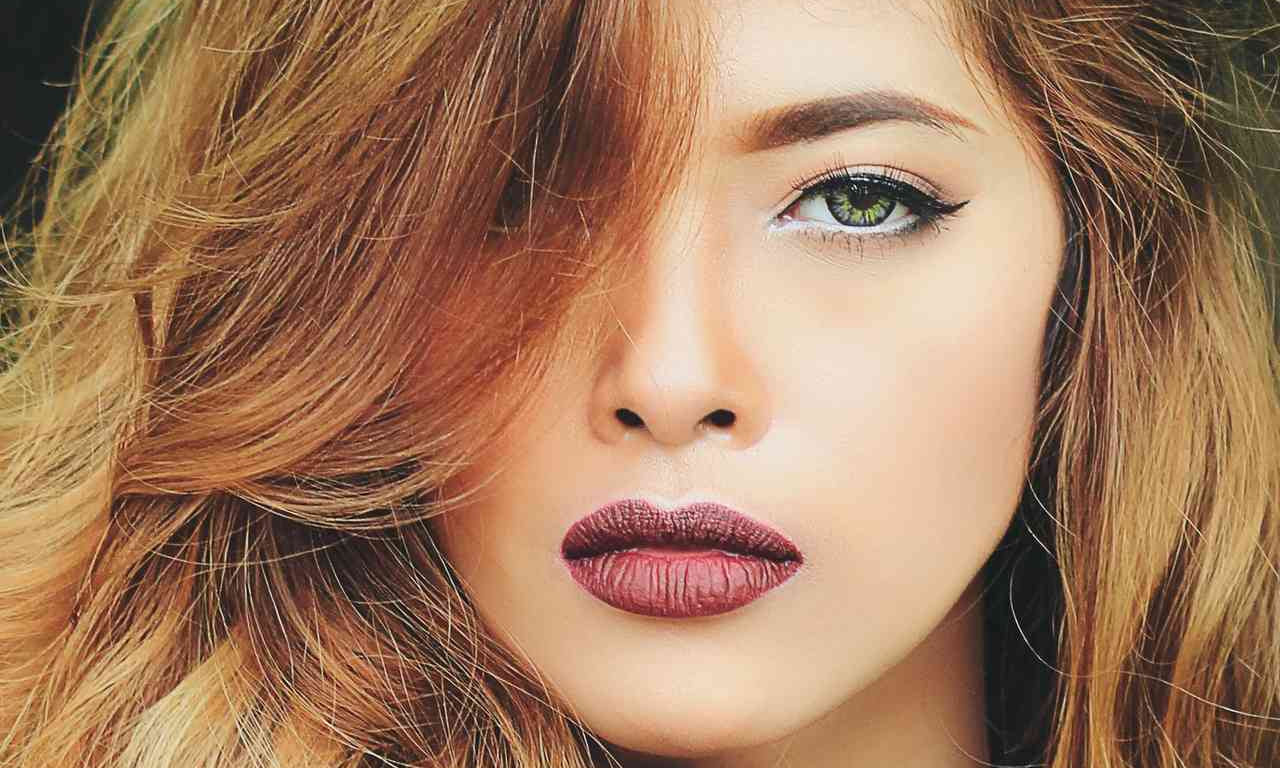 woman with warm golden-brown hair, green eyes, and deep rose lipstick