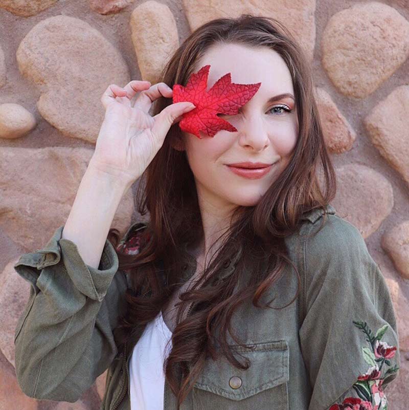 image of woman wearing lipstick for fall covering her right eye with a fall red leaf