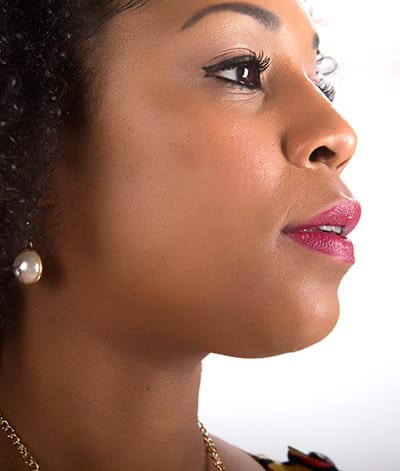 Image of lady with dark skin tone, black hair looking towards her left. She is shown wearing Hibiscus lipstick by Red Apple Lipstick. Hibiscus is a luscious and vibrant true raspberry color. A deep, berry pink with a hint of red.