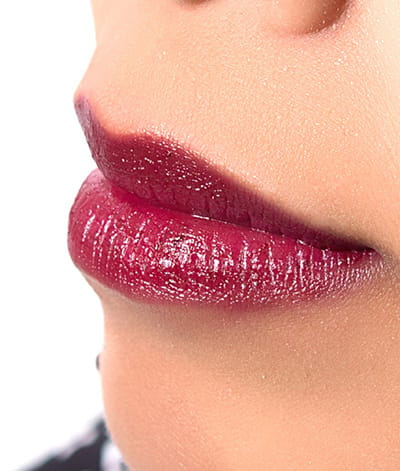Image of close up lips on a lady with medium skin tone. She is featured wearing lipstick in the shade called Wine & Dandy. Though it appears dark in the tube it can be worn either way. If you like a deep vampy look, apply two coats, blotting in between. If you prefer a simple wine stain apply with our lip brush, then blot – it will leave you with a beautiful and light berry stain.