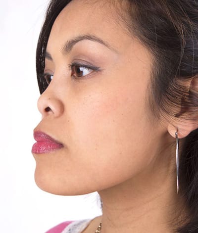 Image of lady with medium skin tone looking to her left with a side view showing her wearing lipstick in the shade called Love My Kiss by Red Apple Lipstick. This lipstick is the perfect middle ground between pink and red.