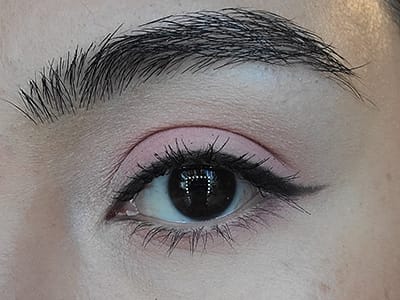 Image of a female eye with dark brown eyes completing the monochromatic pink makeup look having applied The Lash Project mascara.