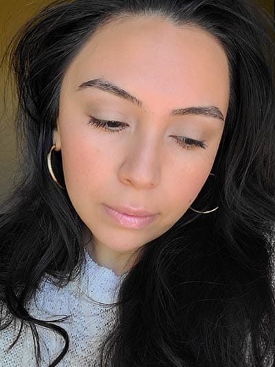 Image of lady with long dark hair, dark eyes and brows with medium skin tone. She is featured here looking to her left and head tilted slightly downward after completing the Ethereal and Natural Summertime makeup look. All with Red Apple lipstick products.