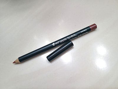 Image of Red Apple Lipstick Natural Lip Liner pencil laying on a table top with the cap off and laying next to it