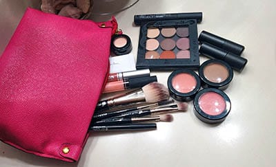 Image of hot pink makup bag with spilled out makeup on a table top. All Red Apple Lipstick products from eyeshadows, Primer, Blushes/Bronzer brush applicators and mascara shown.