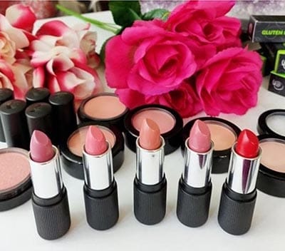 Image of 5 Red Apple Lipsticks with lipstick bullet's twisted up and caps off on a display with some blushes with floral background showing some pinks that make great options for a cream blush