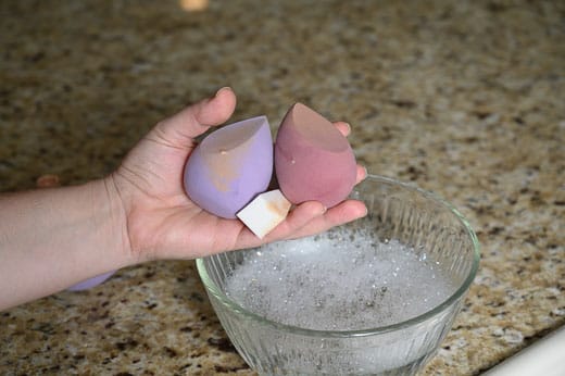 Washing makeup sponges in a bowl of hot water and soap